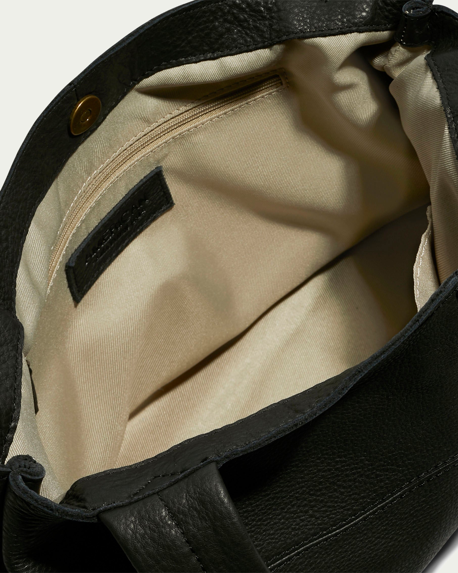 Close-up of an open Virginia Tote by American Leather Co., highlighting the beige fabric interior. Made from luxurious black calf leather, this tote includes a zippered compartment and a small pocket, with a magnetic snap closure at the top.