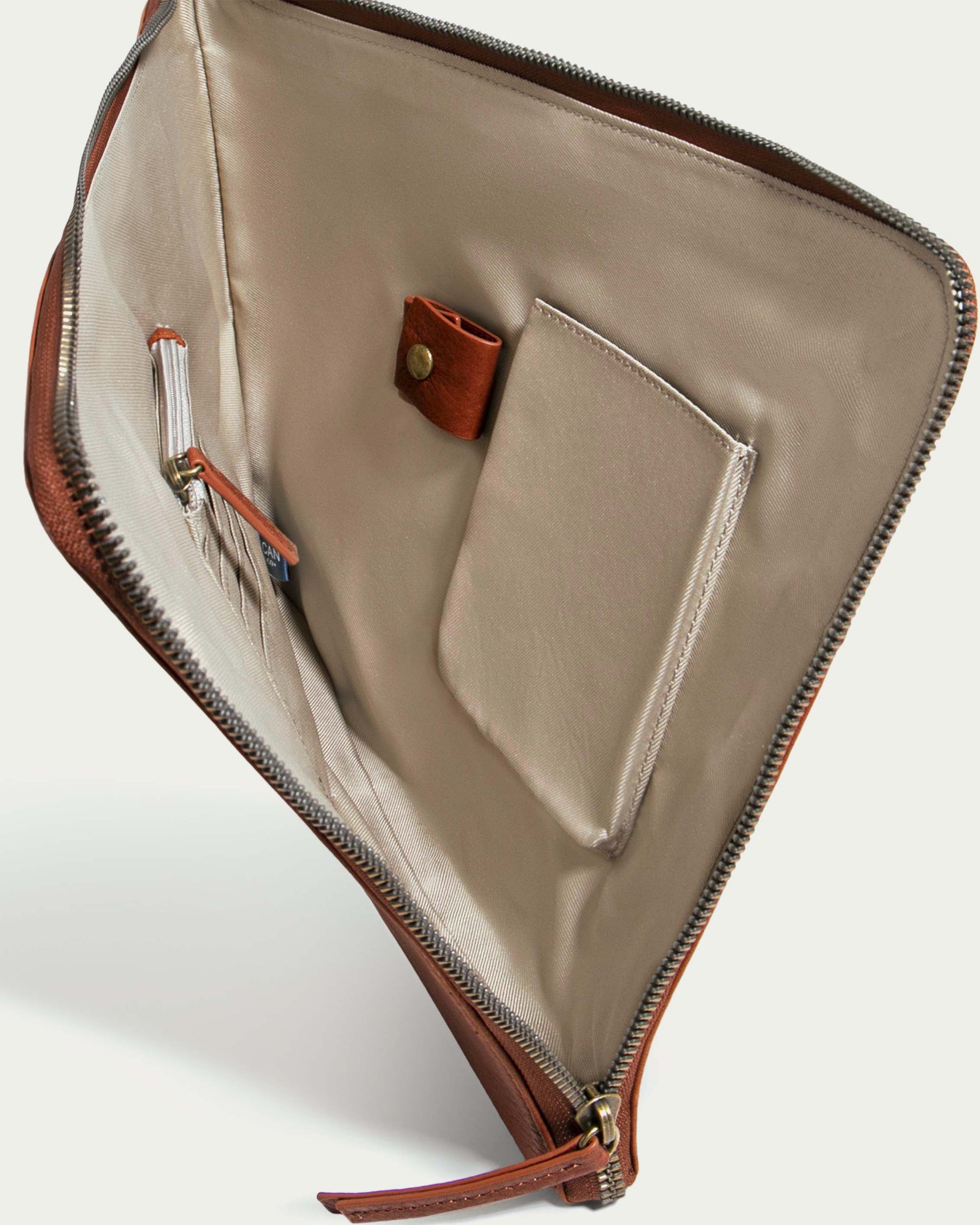 Open Wilmington Tech Organizer by American Leather Co. in brown leather, featuring a zippered closure and a beige interior. It includes a pen holder, pocket, and card slots. Laid flat to showcase its organized compartments, it is an ideal tech case for your essentials.