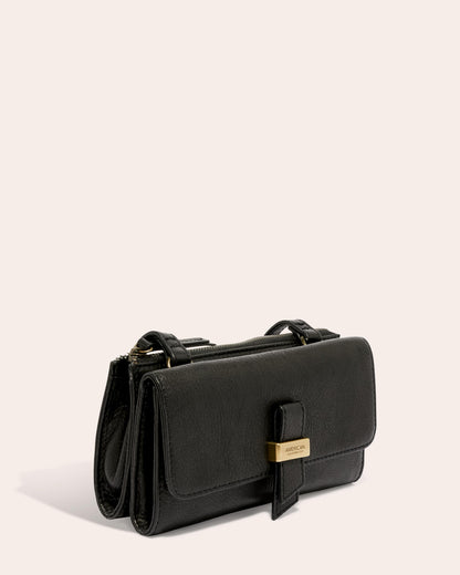 The Essex Wallet Crossbody by American Leather Co. is a chic black leather handbag crafted from genuine American leather. It boasts a rectangular shape with a flap closure, complemented by a gold-colored clasp and small top handle. Photographed against a neutral backdrop, this stylish accessory includes an adjustable crossbody strap for added versatility.