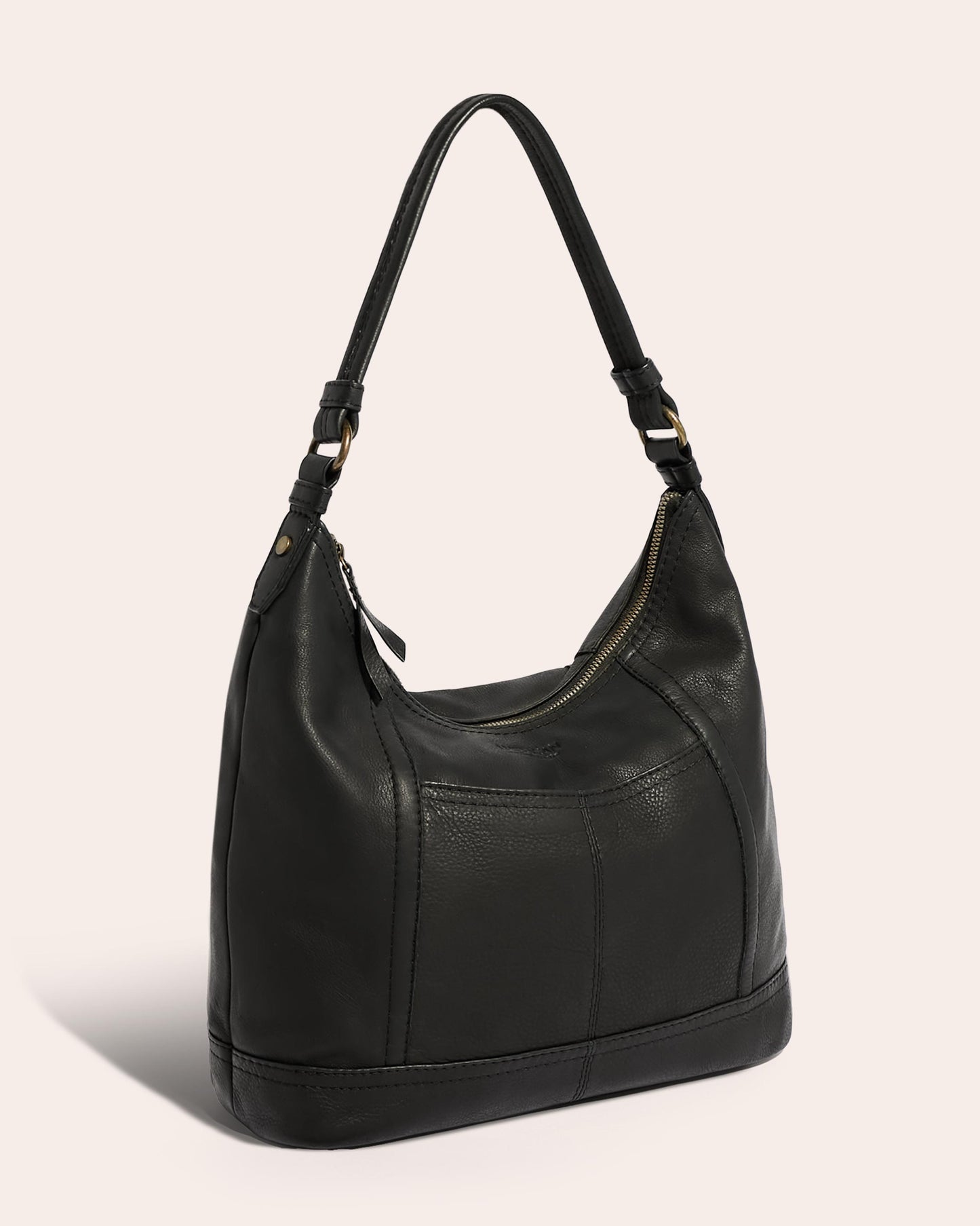 The Hudson Hobo by American Leather Co. is a black leather shoulder bag featuring a single strap and gold-toned, antiqued hardware. This genuine American leather bag has a zipper closure and boasts a slightly slouchy, soft construction. The background is a neutral, pale pink.