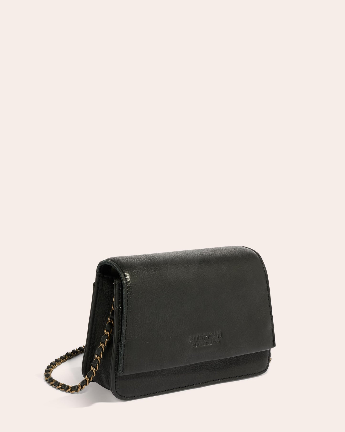 The Liberty Chain Crossbody, a small black purse made from genuine leather by American Leather Co., features a flap closure and a chain crossbody strap. The bag is positioned facing the left on a neutral background.