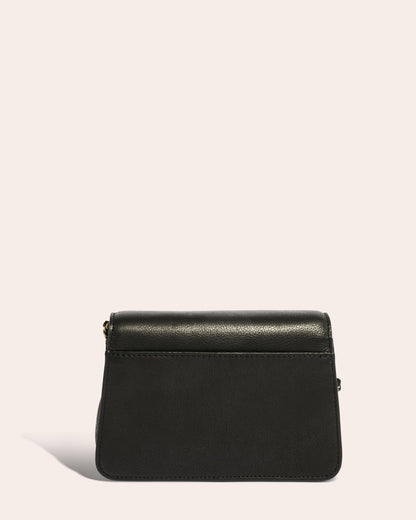 The Liberty Chain Crossbody by American Leather Co. is showcased against a light background. This genuine leather bag, crafted in a sleek rectangular shape with a subtle shine, features a thin strap secured with gold-colored clasps, while shadows cast on the surface enhance the texture of its exquisite craftsmanship.