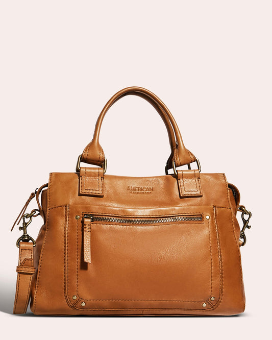 The Jamestown Satchel by American Leather Co. is crafted from genuine American leather and features dual handles along with an adjustable crossbody strap. This tan handbag includes a front zippered pocket, brass hardware, and the brand name embossed on the front. The design boasts multiple stitched details and a spacious interior.