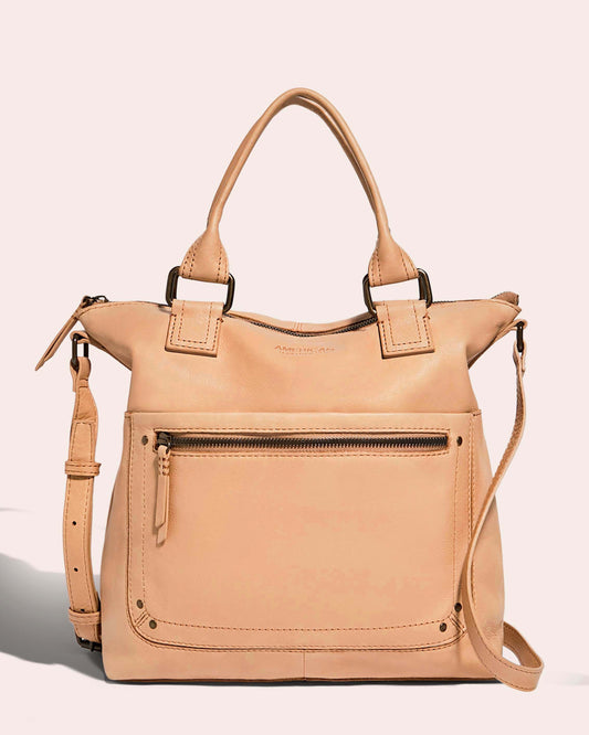 The Jamestown Tote by American Leather Co. is a beige leather bag made from authentic American leather, featuring dual handles and an adjustable shoulder strap. It has a front zippered pocket and a main compartment with zipper closure, all beautifully complemented by its neutral background.